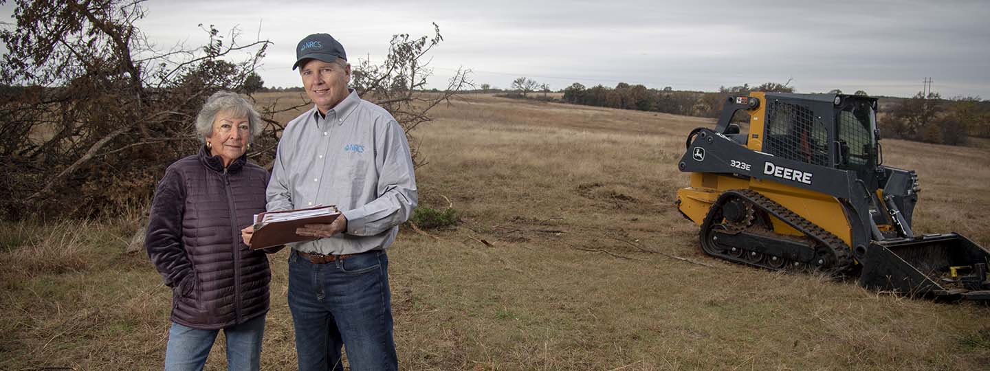 two people referring to a report in a field with farm equipment